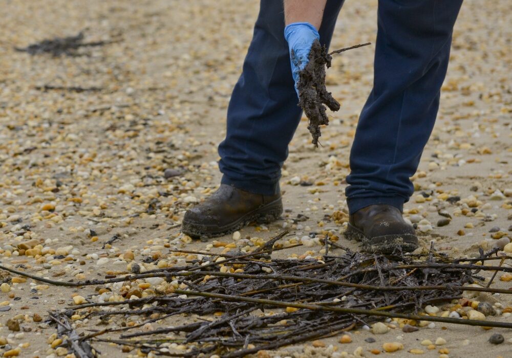 A member of a contracted oil spill response organization cleans oily debris from Slaughter Beach in Delaware as part of the Broadkill 2020 oil spill response. The Coast Guard and the Delaware Department of Natural Resources and Environmental Control are working together to identify areas where tar balls and oily debris are making landfall to facilitate an effective clean up.(U.S. Coast Guard photo by Petty Officer 3rd Class Isaac Cross.)